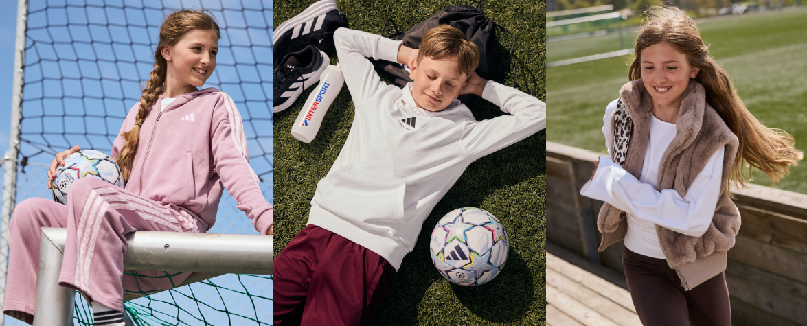 Tre børn i fritids- og sportstøj ved en fodboldbane: pige i rosa træningssæt, dreng liggende på græs med bold, pige i beige vest løbende.